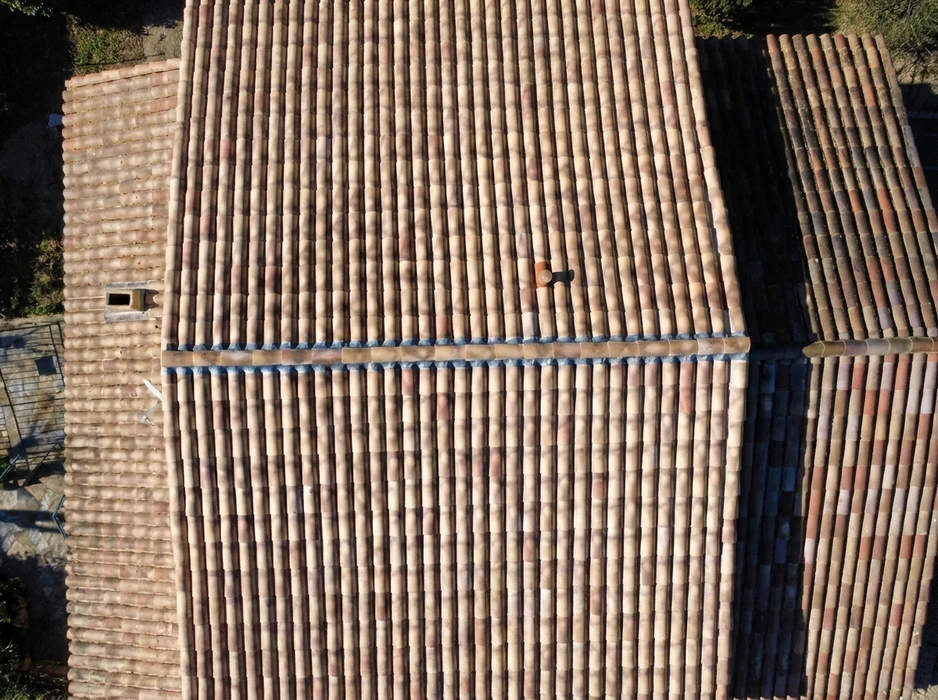 Vue aérienne d'une toiture en tuiles canal terre cuite, composée de deux versants séparés par un faîtage horizontal