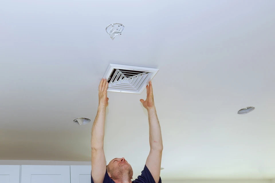 Un technicien installe ou répare une bouche d'aération carrée au plafond d'un intérieur résidentiel