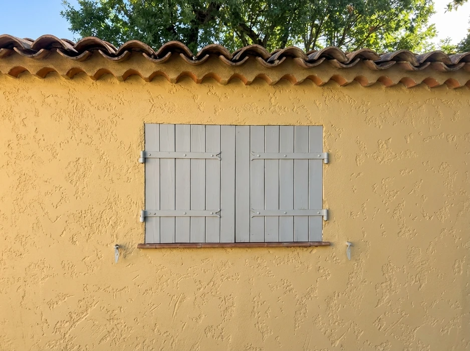 Façade extérieure d'une maison méditerranéenne, mur en crépi jaune ocre, toiture en tuiles canal
